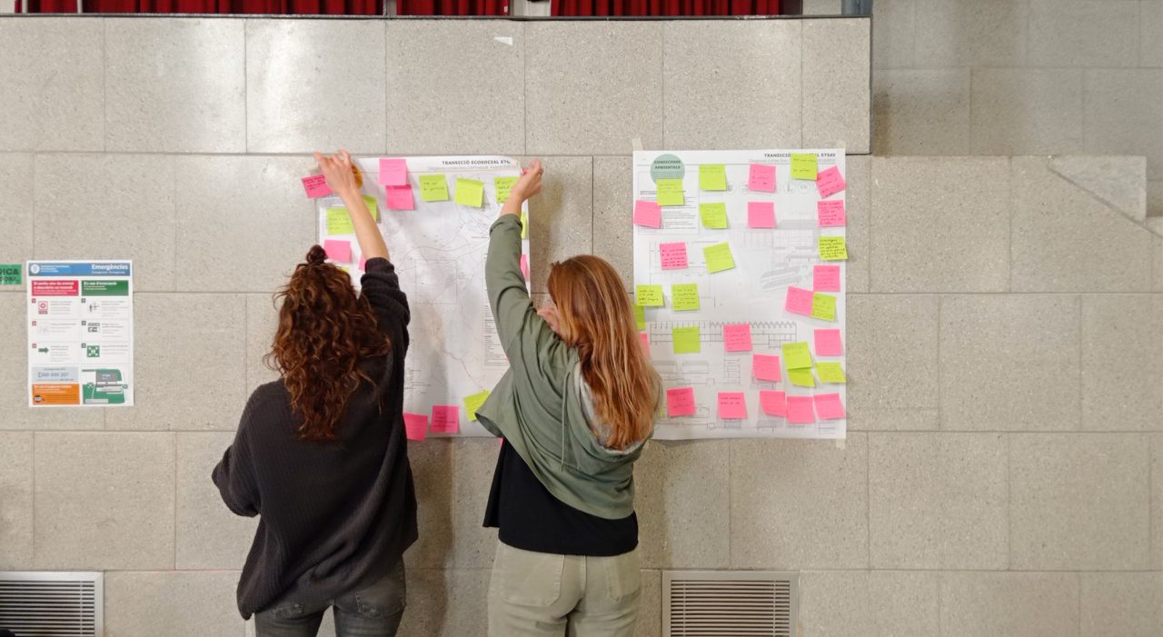 Dues noies pengen postits amb notes en un mural
